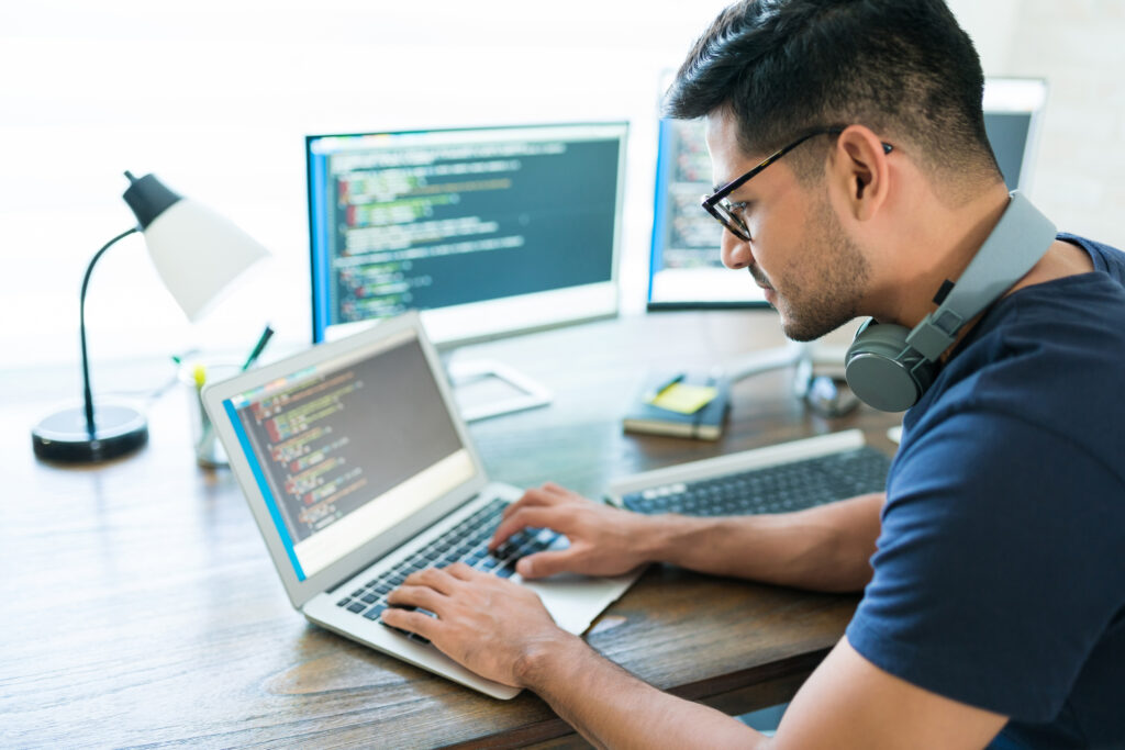 Homem digital no notebook com duas telas de computador atrás mostrando códigos de tecnologia
